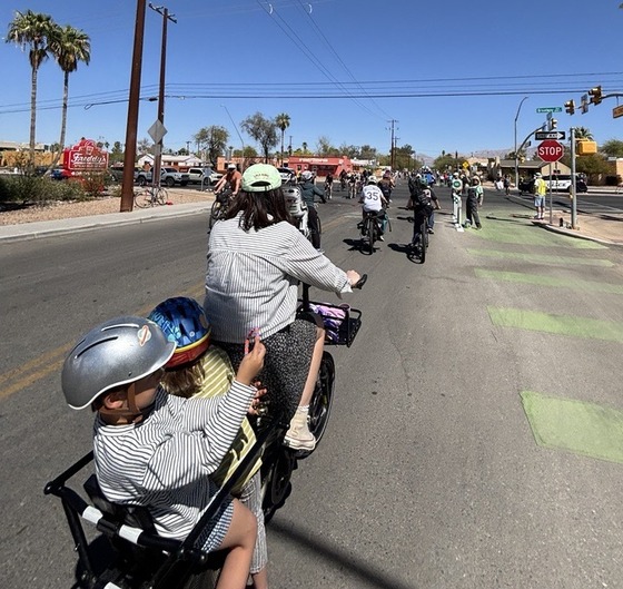 Photo of Chelsea Blue with two cute kids on her cargo bike and car free streets ahead.
