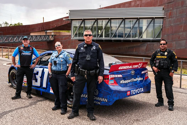 Officers stand for a group photo in front of a race car.