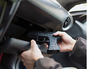 Hands remove a pistol from a glove compartment.