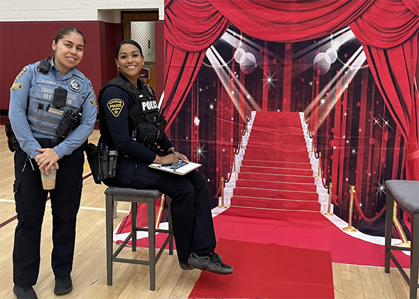 A female TPD officer and a female TPD CSO pose in front of a "red carpet" backdrop, apparently waiting to do an interview.