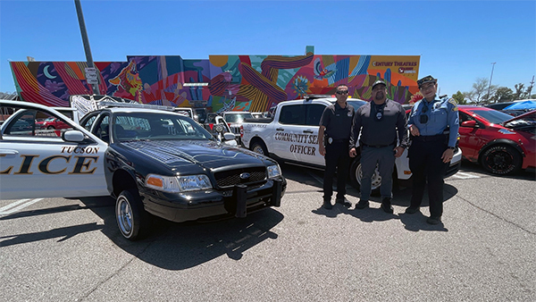 Two police officers and one CSO in uniform stand in front of patrol cars in a Century Theater parking lot.