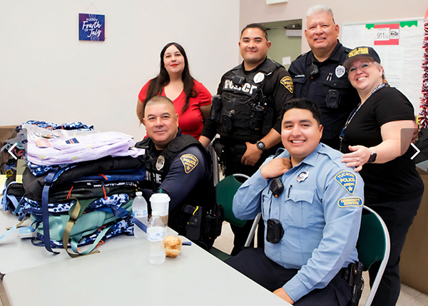 Officers and CSOs behind a table with a stack of backpacks on it.