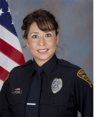 Department photo of smiling female officer in uniform in front of an American flag.
