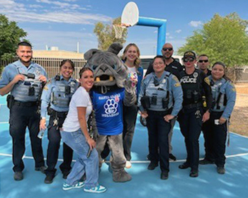 Uniformed and school personnel pose for a group photo outside on a basketball court.