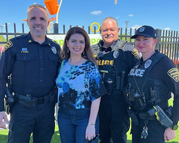 Group photo outdoors in front of a splash pad with 3 uniformed officers, including Captain Flores, and Mayor Romero.