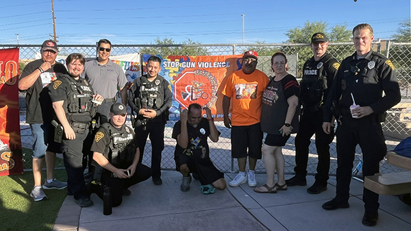 Uniformed officers and community members pose for a group photo outside in front of a chain link fence.