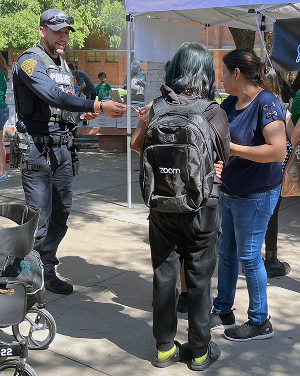 An officer in uniform hands a card to a student. They are outside at a resource fair.