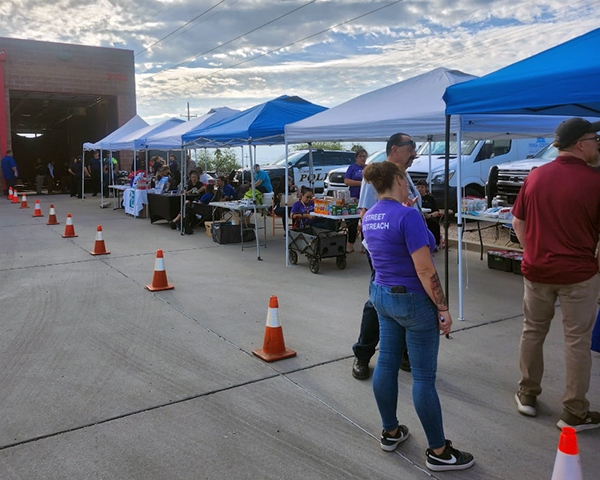 Information tables set up outside a fire station in the early morning. People are staffing and visiting the tables.