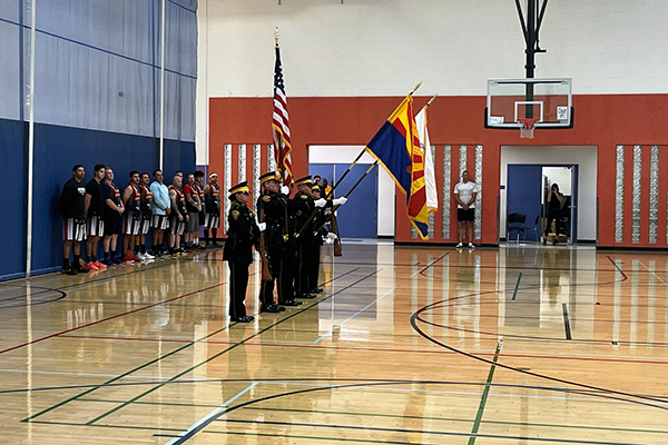 Honor guard members hold flags on basketball court. Team members are seen in the background.