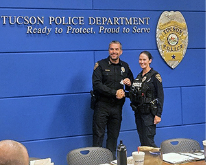 Female officer shakes hands with Chief of Police in front of a wall that reads Tucson Police Department Ready to Protect, Proud to Serve.