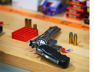 Barcode-tagged handgun on laboratory bench, bullets nearby.