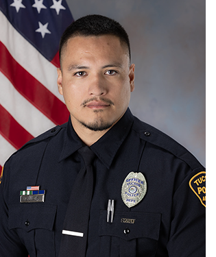 Department portrait of uniformed male officer in front of an American flag.