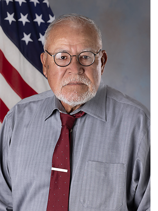 Department portrait of a male in office attire in front of an American flag.