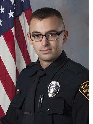 Department portrait of male officer in uniform in front of an American flag.
