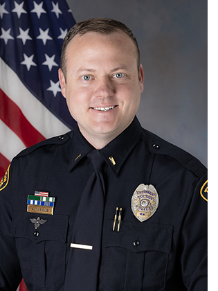 Department portrait of male lieutenant in uniform in front of an American flag.