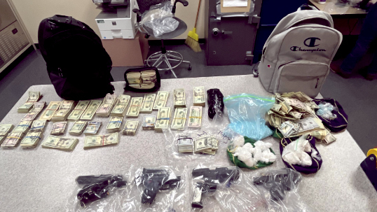 Seized narcotics, guns, and cash displayed on a tabletop in an office.