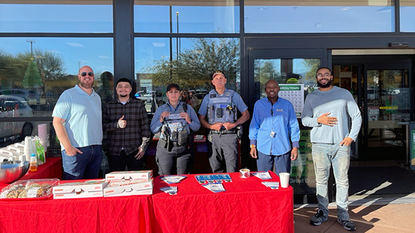 Group photo of officers and CSOs in uniform standing behind a table with pastries and coffee outside Nordstrom Rack.