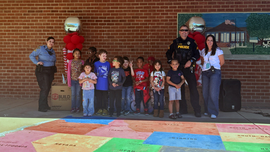 Children and a school staff member stand with a uniformed officer and CSO outside a school for a group photo.