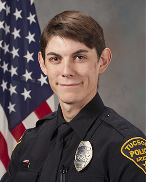 Department portrait of officer in uniform in front of an American flag.