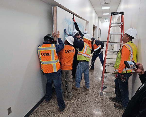 Construction workers in hard hats and safety vests struggle to place the mural in its new home.