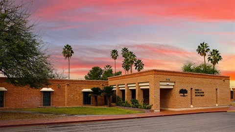 The City of Tucson Parks & Recreation Department headquarters building at sunset, with palm trees and a vivid pink and orange sky in the background.