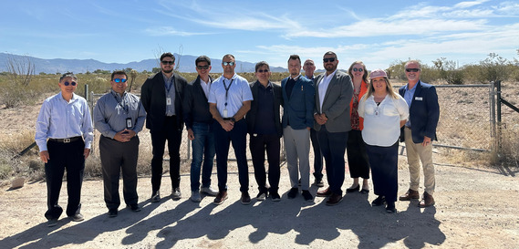 Twelve men and women standing outside in front of a chain link fence