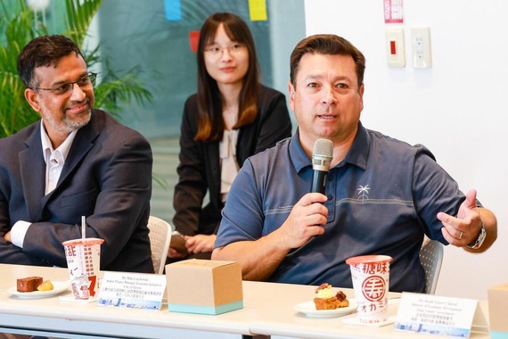 Mike Czechowski speaking into a microphone while sitting at a table with a man and woman to his left