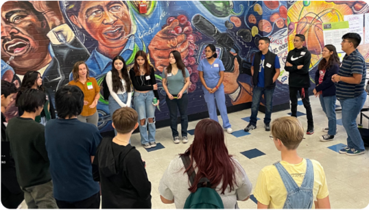 Photo of Kids at the Tucson Youth Climate Action Fund standing together in a circle in front of a mural.