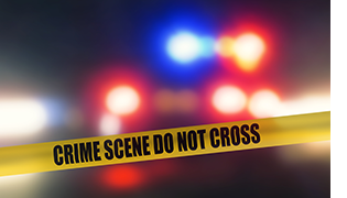 "CRIME SCENE DO NOT CROSS" tape at night with blurry red and blue police lights in the background.