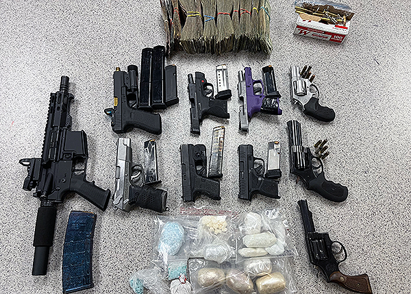 Multiple guns, drugs in baggies, and cash spread out on a table.