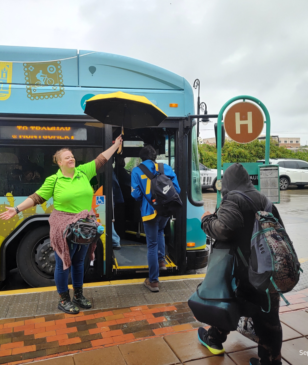 A Transit Ambassador holding an umbrella for riders
