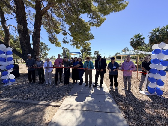 a dozen people stand behind a large red ribbon being cut with extra large scissors at Jacobs Park