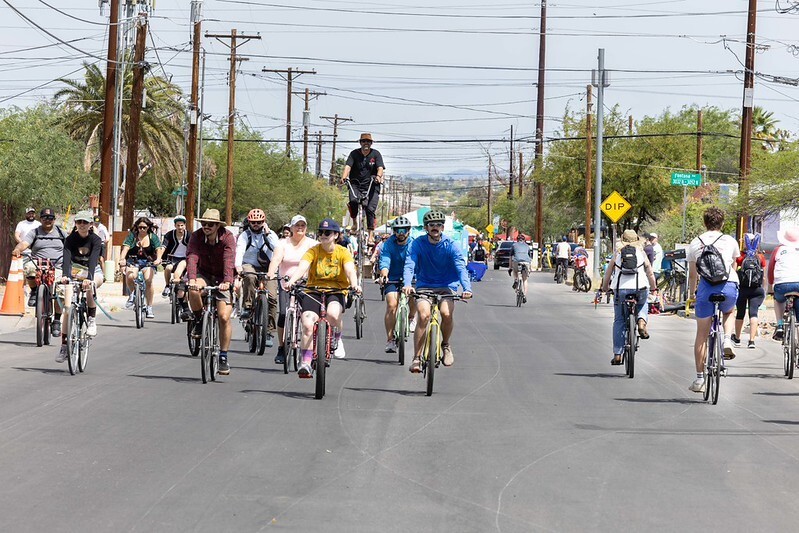 a group of 40 or more cyclists ride through a car-free Tucson street under powerlines with trees in the background