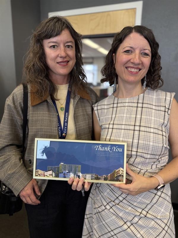 Miranda and Johanna holding a commemorative photo collage of all the projects Johanna worked on