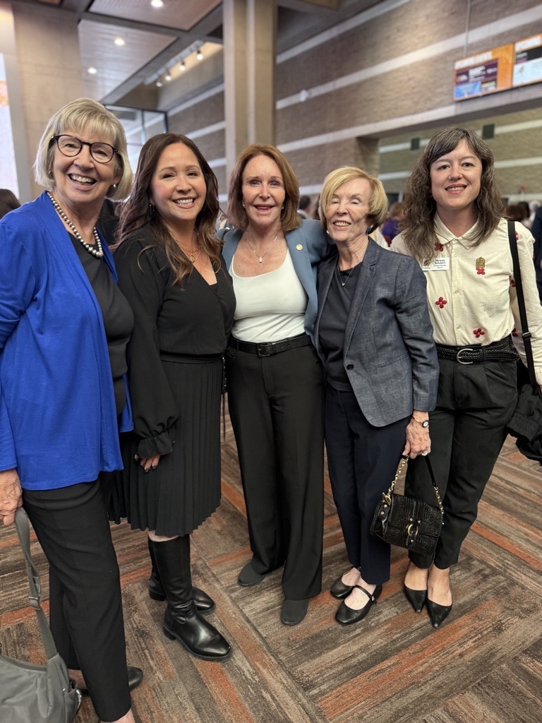 women in business attire smiling and linking arms for photo