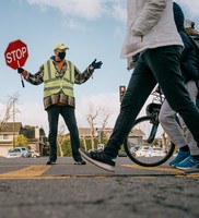 Crossing guard with a mask on, legs and feet of people crossing the street