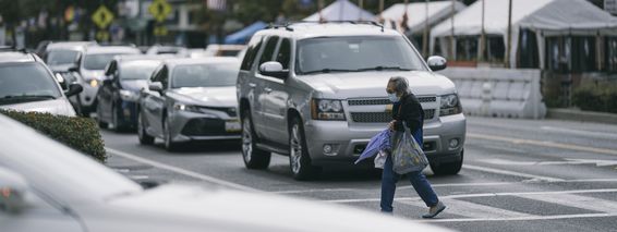Petite elderly woman walks in a crosswalk, where a very large vehicle is stopped