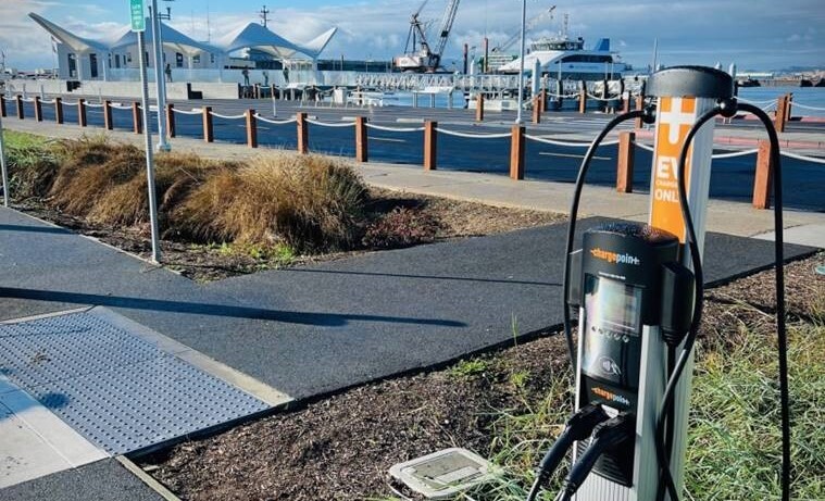 Photo of an EV charger with a ferry terminal and ferry boat in the background