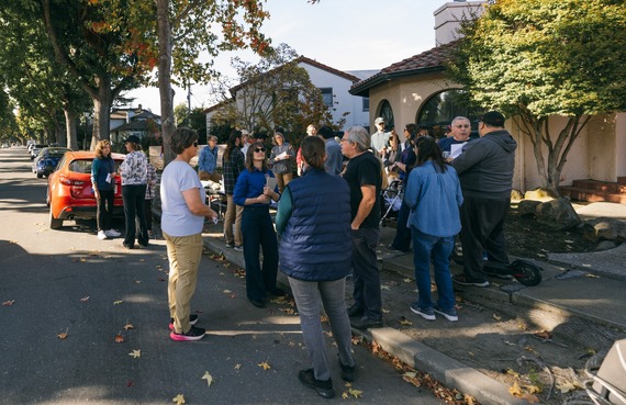 A crowd of people stand outside on Gibbons Dr, talking in small groups