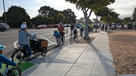 A long line of children and adults on bicycles arrives at a school campus