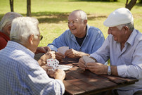 group of elderly men laughing playing a card game outside on a picnic table