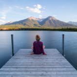A picture of Calm - woman sitting on dock looking out over a quiet lake at sunrise