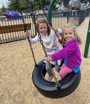 Two kids playing on a tire swing at the park