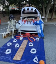 Child  in a shark costume standing next to a pirate and ocean decoration