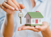 A person holding up a house key and a small model home replica 