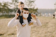 man wearing face covering while carrying child on shoulders