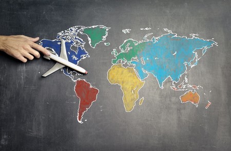Hand holding model airplane flying over chalkboard map of the world