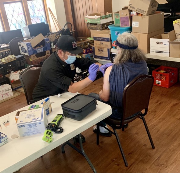 Photo of a Culver City Fire Captain giving the COVID-19 vaccine to a man seated at a table in Grace Lutheran Church.