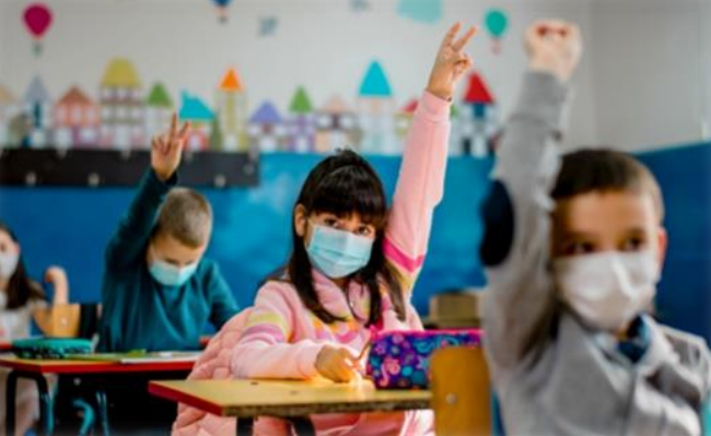 School children raising their hands in class while wearing face covering