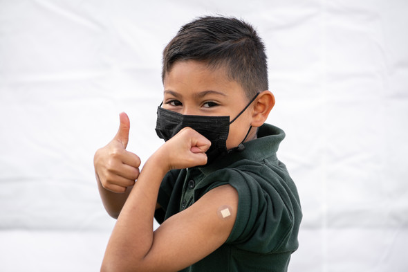 Boy giving "thumbs up" sign while flexing his arm to show he got the COVID-19 vaccination.